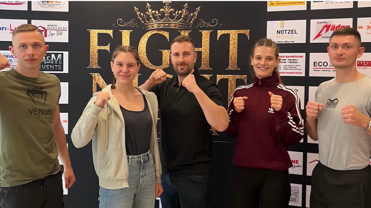 Das Team der KickFit Academy Jena vor der Sponsorenwand der Fight Night Gotha, fünf Personen mit erhobenen Fäusten.